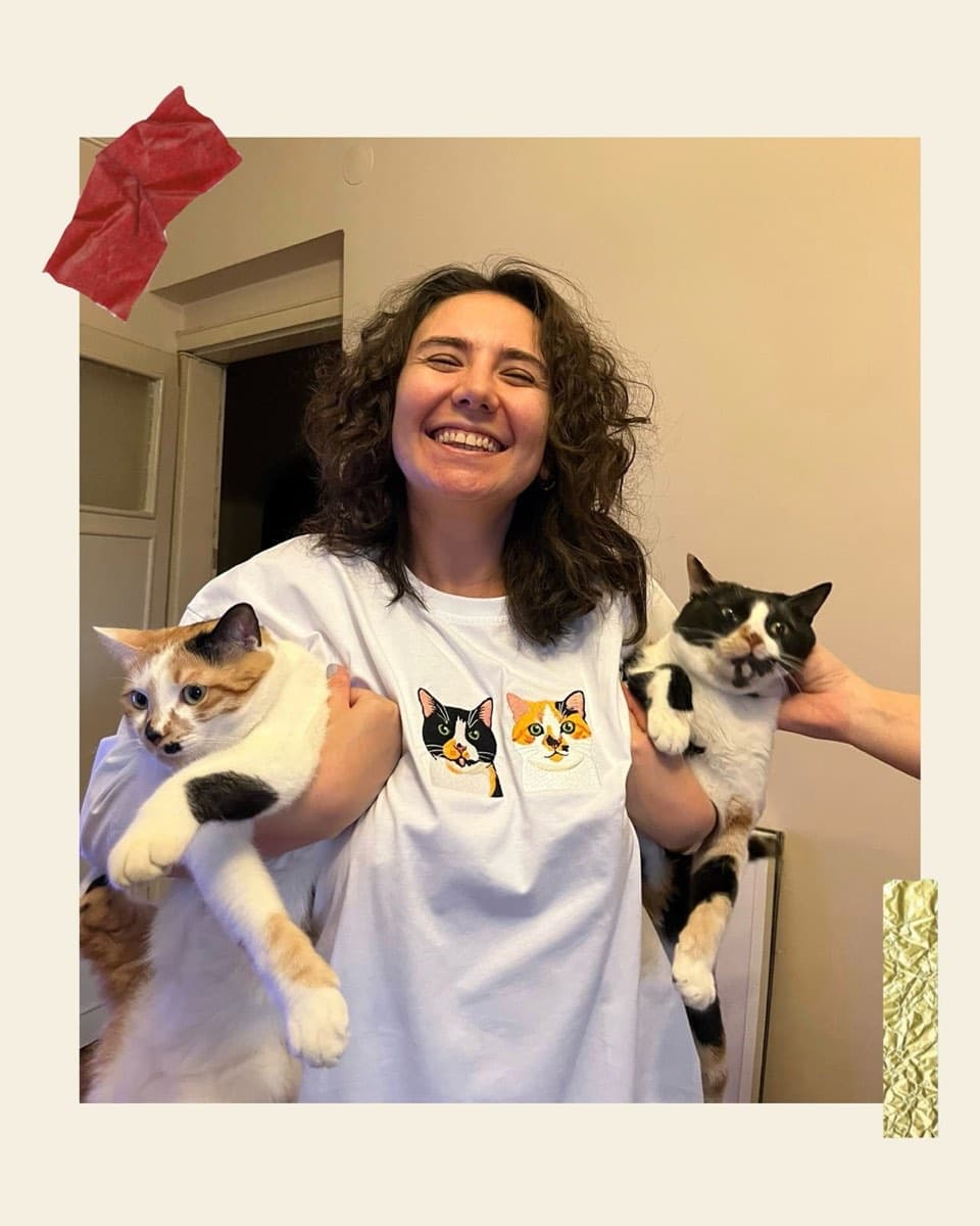 Müşteri, iki kedisiyle birlikte kedi nakışlı beyaz tişörtünü giyerken